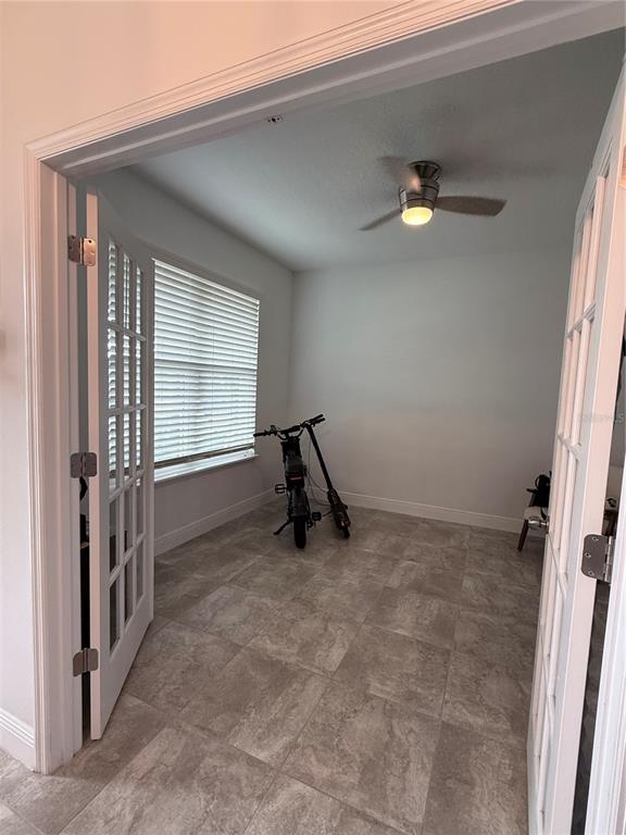 A room with tile flooring, a ceiling fan, and French doors, containing two electric scooters — 8386 IRON MOUNTAIN TRAIL, WINDERMERE, FL