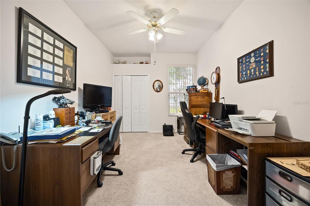 A home office features two wooden desks, a ceiling fan, and carpeted flooring — 4122 KINGSLEY STREET, CLERMONT, FL