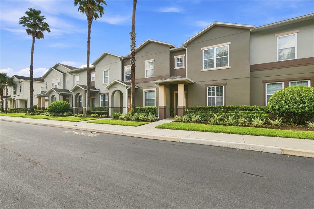 A row of two-story townhomes with tan stucco exteriors and palm trees along the street — 829 BELLES FERRY LOOP, SANFORD, FL