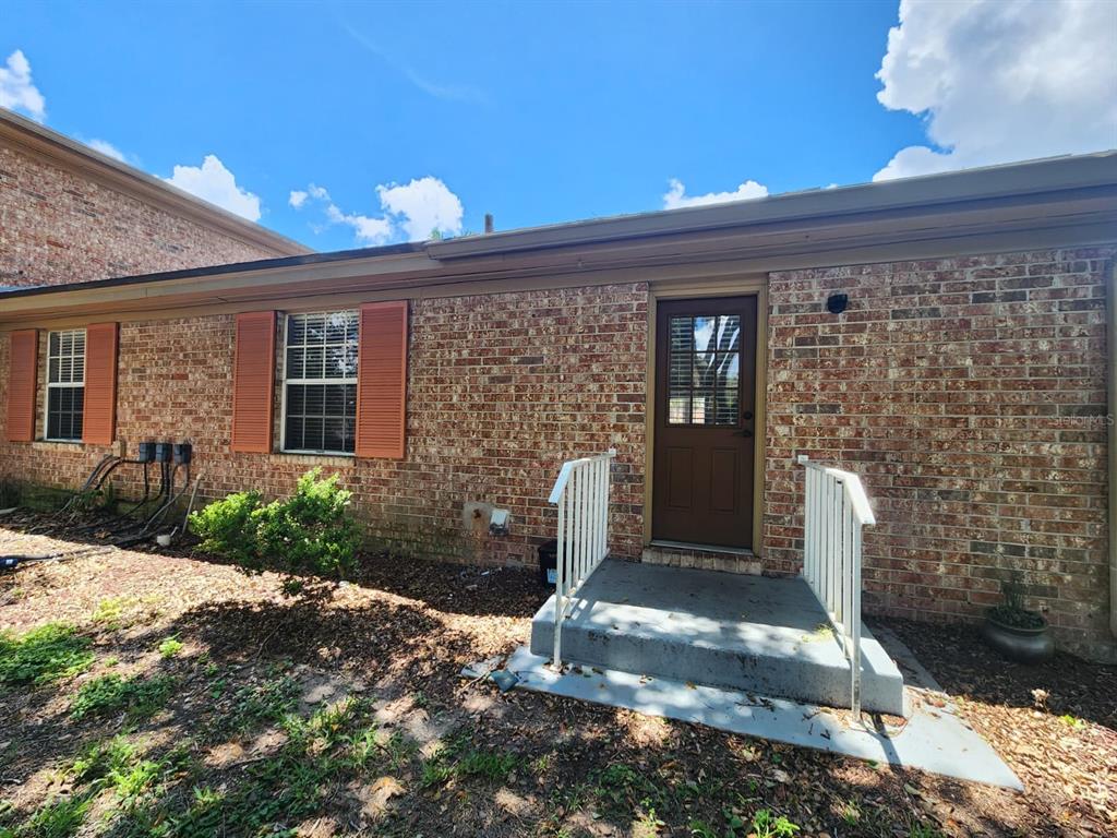 A brick exterior wall features two windows with orange shutters and a single entry door — 416 BANYON TREE CIRCLE UNIT 108, MAITLAND, FL