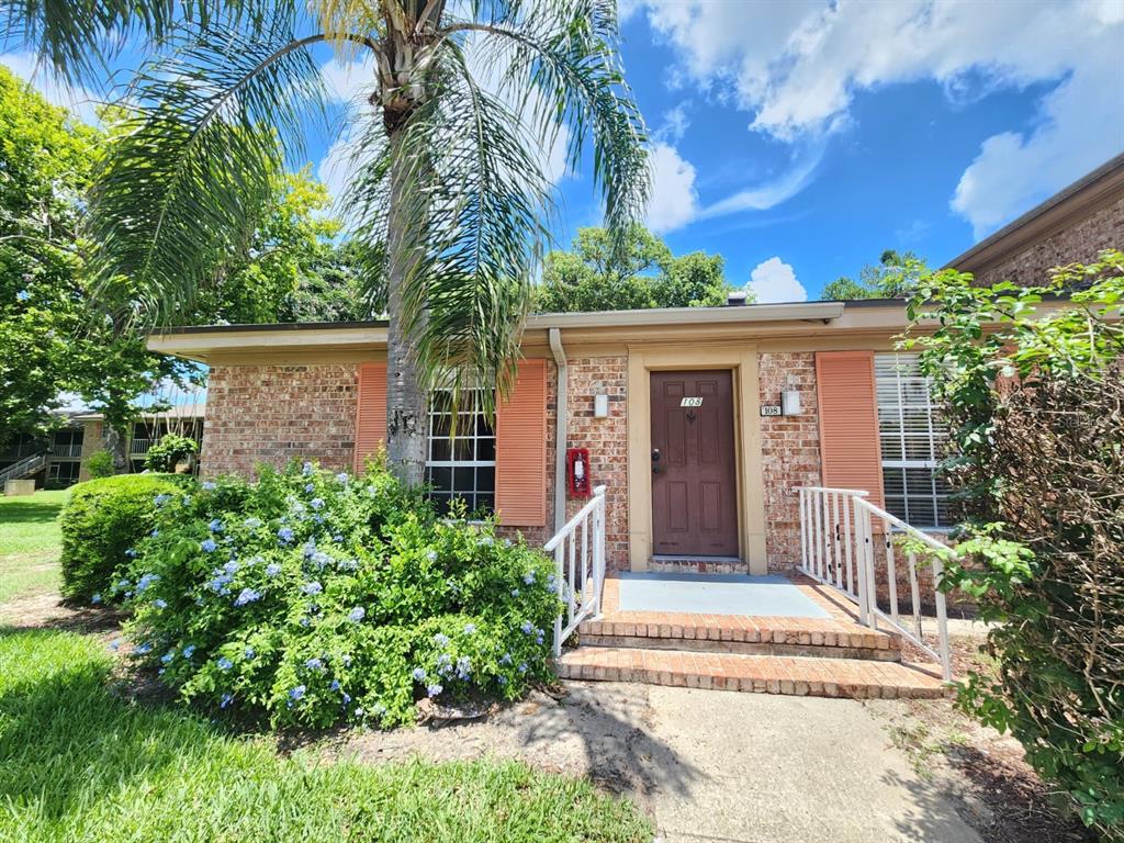 A brick exterior of a single-story building features a brown front door and a palm tree — 416 BANYON TREE CIRCLE UNIT 108, MAITLAND, FL