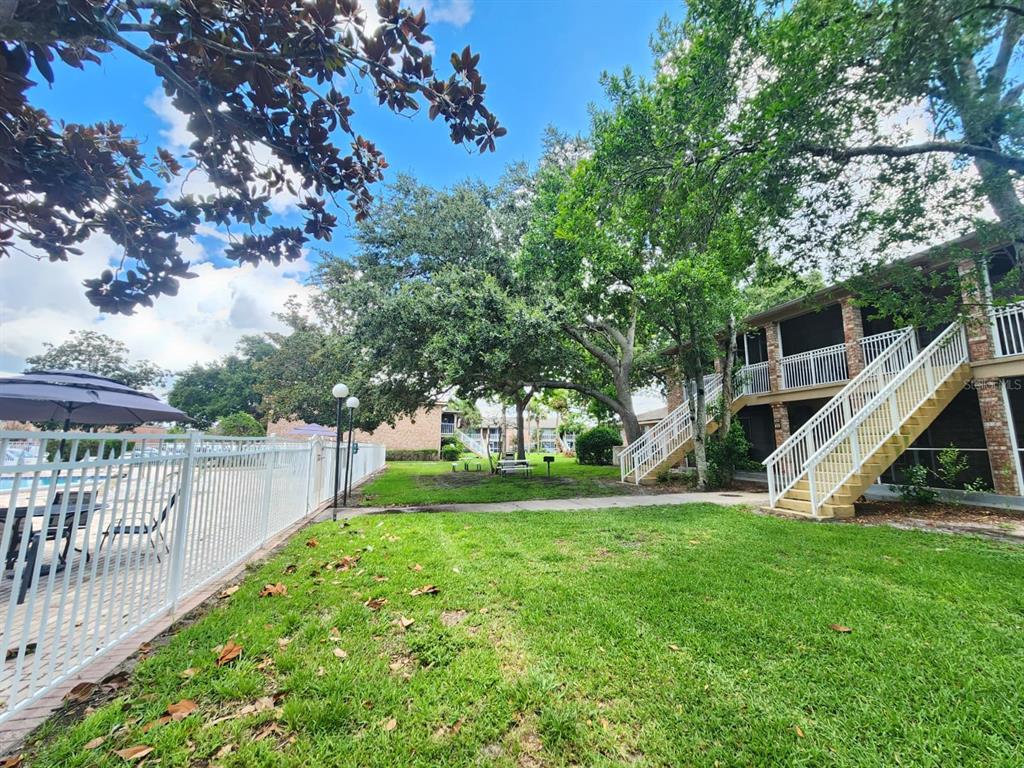 A grassy courtyard with trees, a white fence, and an outdoor staircase to apartment units — 416 BANYON TREE CIRCLE UNIT 108, MAITLAND, FL
