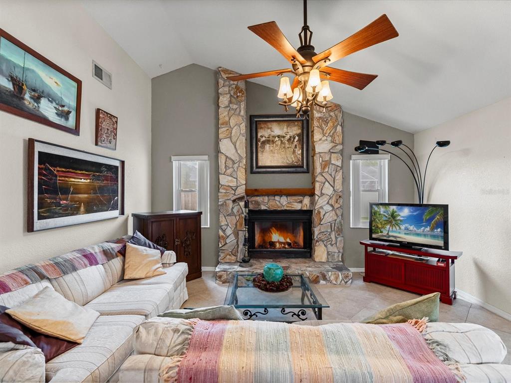 A living room features a stone fireplace, a ceiling fan, and a television on a stand — 12595 93RD WAY, LARGO, FL