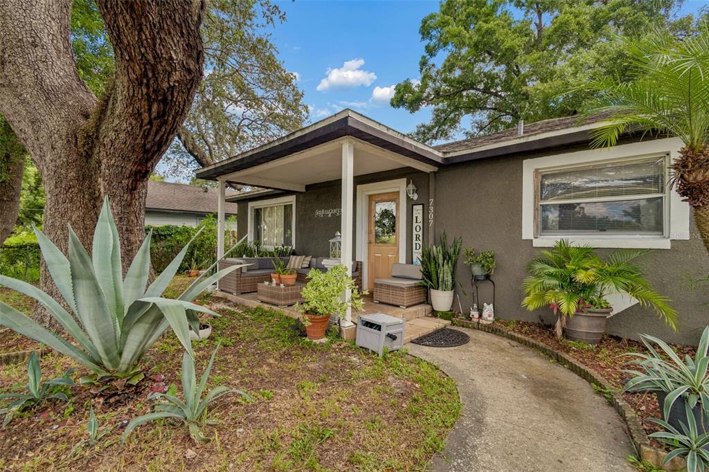 A single-story house with a covered front porch, a concrete walkway, and various potted plants — 7307 N HUNTLEY AVENUE, TAMPA, FL
