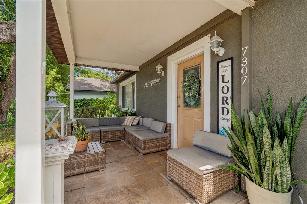 A covered front porch features stone flooring, wicker sectional seating, and a decorative wooden sign — 7307 N HUNTLEY AVENUE, TAMPA, FL