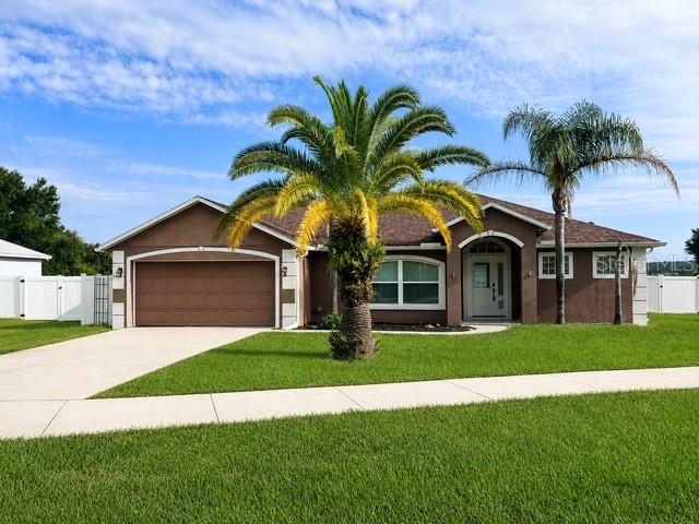 A brown single-story house with a two-car garage and two palm trees in the front yard — 309 GENTLE BREEZE DRIVE, MINNEOLA, FL