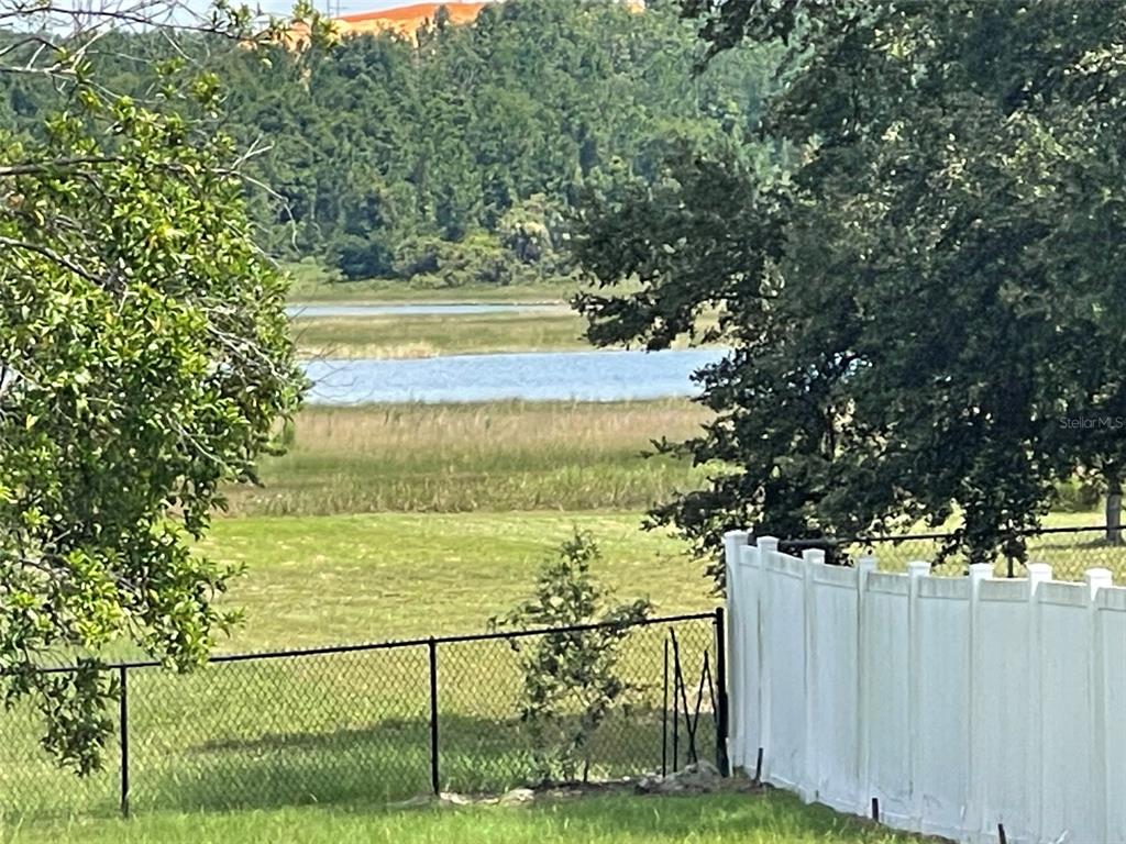 A view of a grassy yard, a chain-link fence, a white privacy fence, and a lake — 309 GENTLE BREEZE DRIVE, MINNEOLA, FL