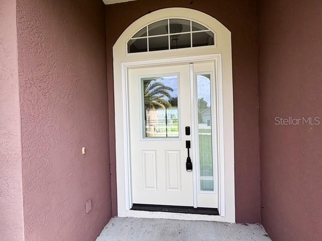 A white front door with a glass insert and arched transom window sits between brown walls — 309 GENTLE BREEZE DRIVE, MINNEOLA, FL