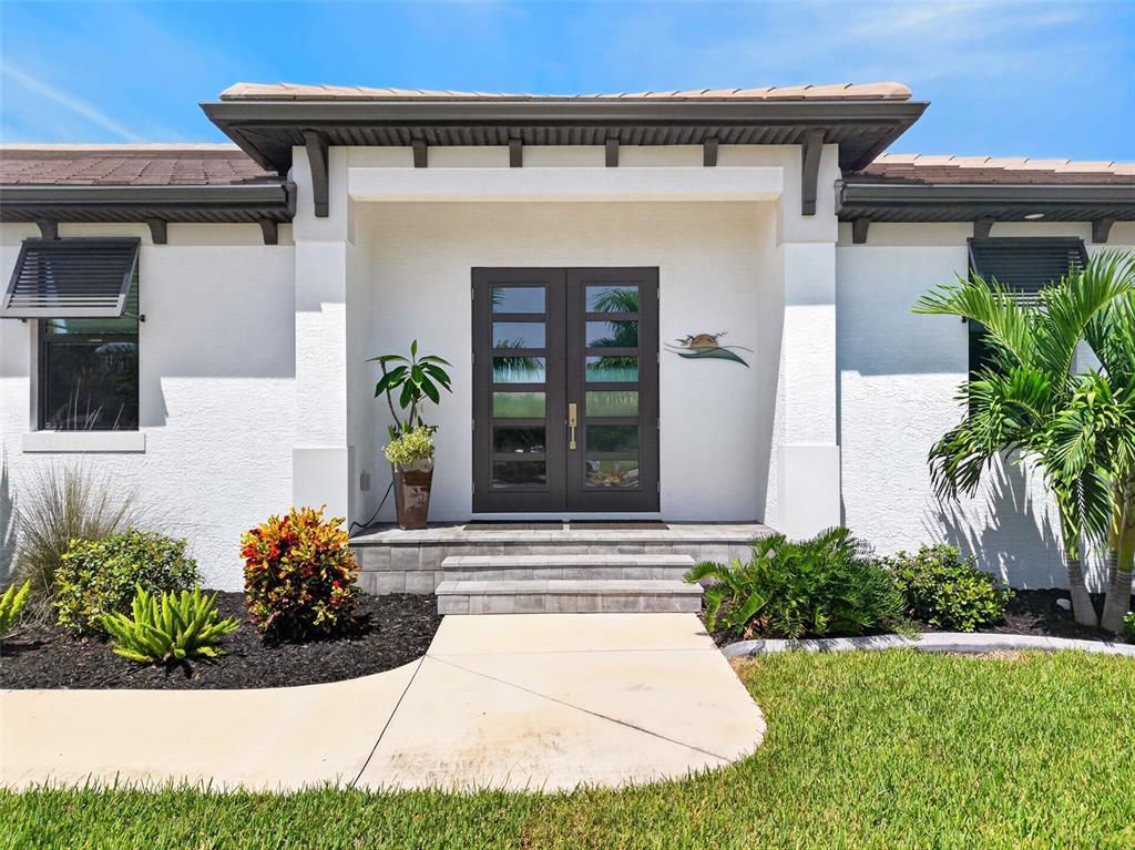 The exterior of a house features a white stucco facade, dark double doors, and landscaping — 1737 CASEY KEY DRIVE, PUNTA GORDA, FL
