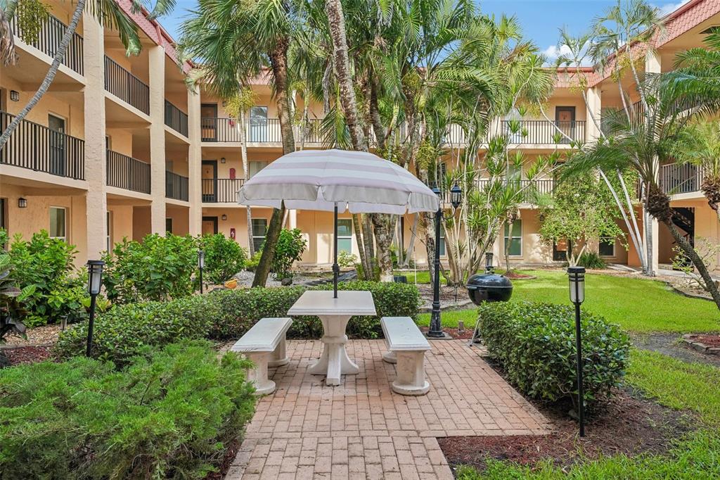 A brick patio with a table, benches, and umbrella sits in a courtyard between apartment buildings — 8911 BLIND PASS ROAD UNIT 319, ST PETE BEACH, FL