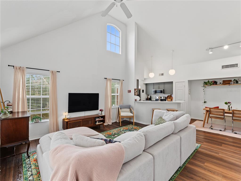 A living room with vaulted ceilings, a large sectional sofa, and an open kitchen area — 9186 LAKE CHASE ISLAND WAY, TAMPA, FL