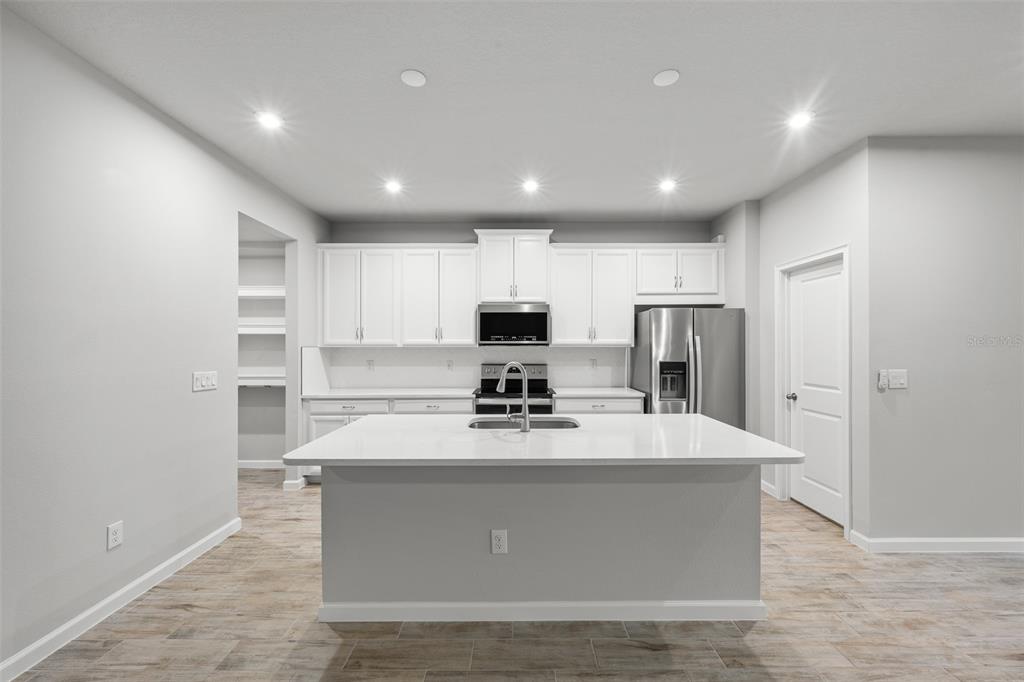 An open-concept living room and kitchen featuring light wood flooring and modern furniture — 4366 CLOUD HOPPER WAY, LUTZ, FL