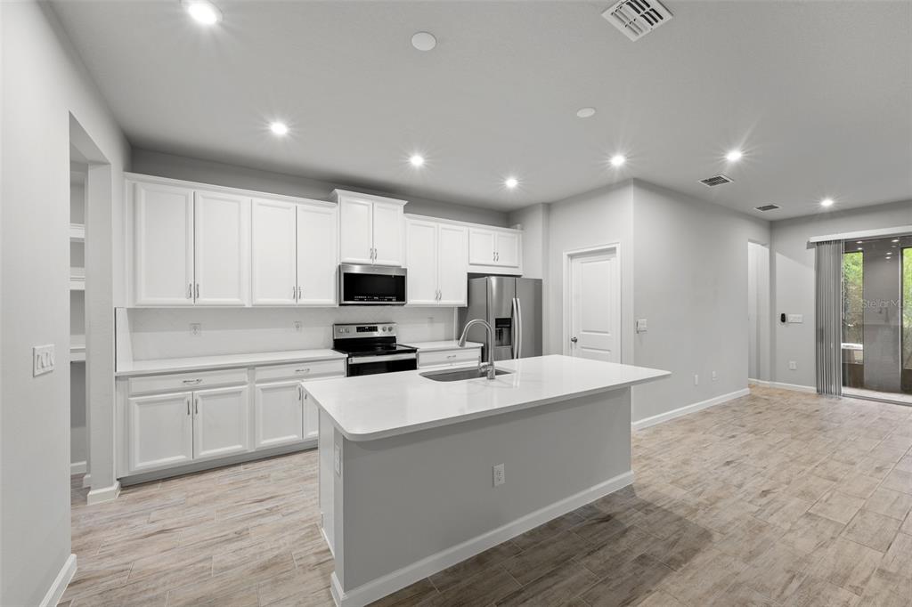 A modern kitchen features white cabinetry, stainless steel appliances, a center island, and tile flooring — 4366 CLOUD HOPPER WAY, LUTZ, FL