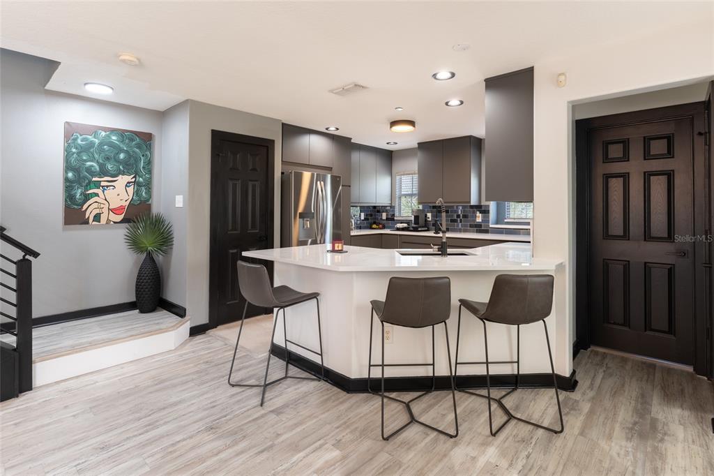 A modern kitchen features dark gray cabinetry, a white peninsula with bar stools, and wood-look flooring — 528 VINCINDA CREST WAY, TAMPA, FL