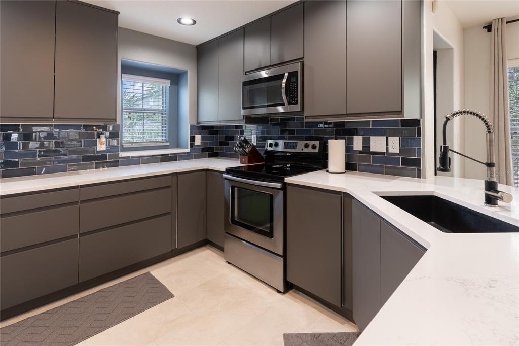 A modern kitchen features dark gray flat-panel cabinets, white countertops, and a blue subway tile backsplash — 528 VINCINDA CREST WAY, TAMPA, FL