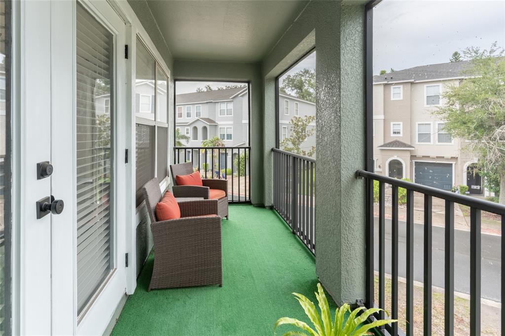 A covered balcony with green outdoor carpeting, two wicker chairs, and black metal railings — 528 VINCINDA CREST WAY, TAMPA, FL
