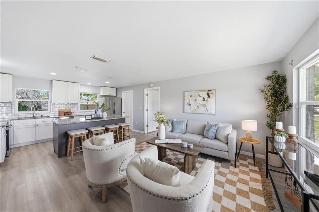 An open-concept living room and kitchen featuring light wood floors and a checkered area rug — 3568 4TH AVENUE SE, LARGO, FL