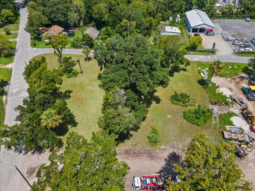 An aerial view shows a grassy, tree-filled vacant lot bordered by roads and commercial buildings — 919 TOMOKA RD, DAYTONA BEACH, FL
