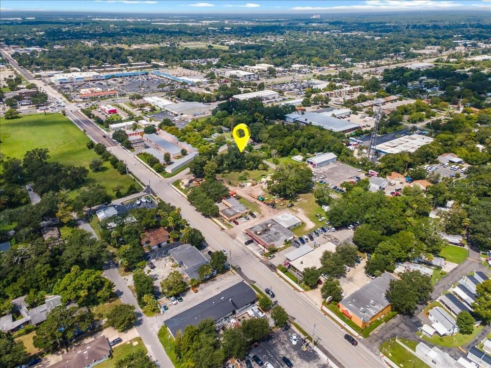An aerial view shows a yellow location pin over a wooded lot near commercial buildings — 919 TOMOKA RD, DAYTONA BEACH, FL