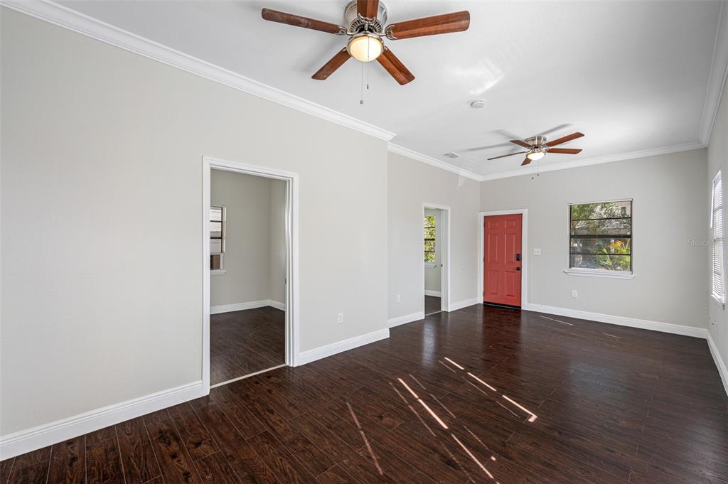 An empty living room features dark wood-look flooring, light gray walls, two ceiling fans, and a red door — 2118 W PALMETTO STREET, TAMPA, FL