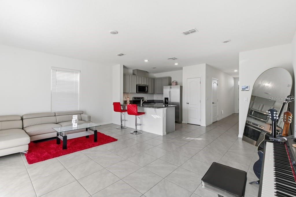 An open-concept living room and kitchen featuring light tile floors, a red rug, and stools — 1727 WOODEN STREET, DAVENPORT, FL