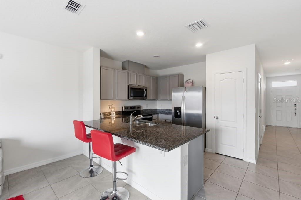 A kitchen features granite countertops, stainless steel appliances, grey cabinetry, and two red bar stools — 1727 WOODEN STREET, DAVENPORT, FL