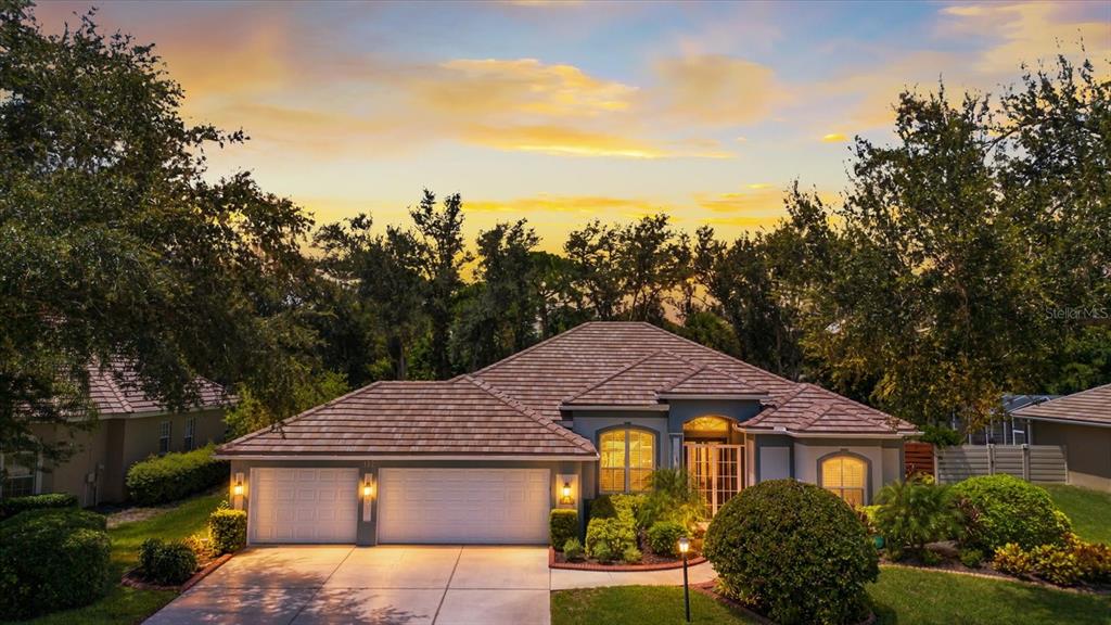 A single-story house with a two-car garage and a tiled roof at sunset — 144 PARK TRACE BOULEVARD, OSPREY, FL