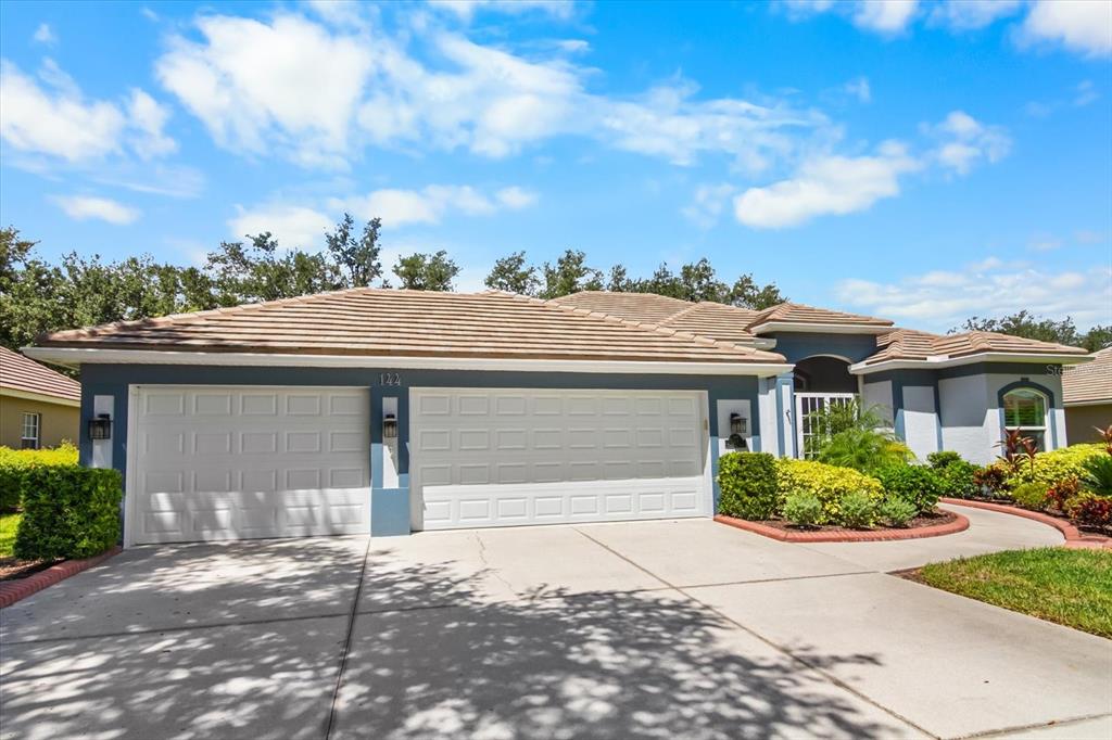 A single-story house with a three-car garage, tan tile roof, and blue exterior trim — 144 PARK TRACE BOULEVARD, OSPREY, FL