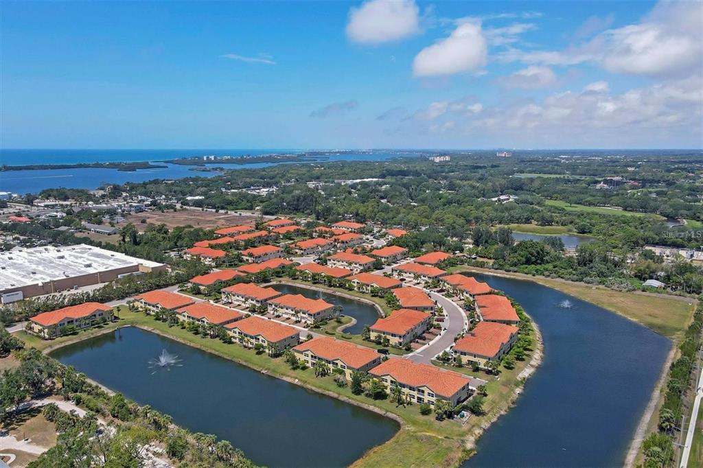 An aerial view shows a residential complex with red-tiled roofs surrounding a central pond — 4219 FRONTIER WAY UNIT 105, OSPREY, FL