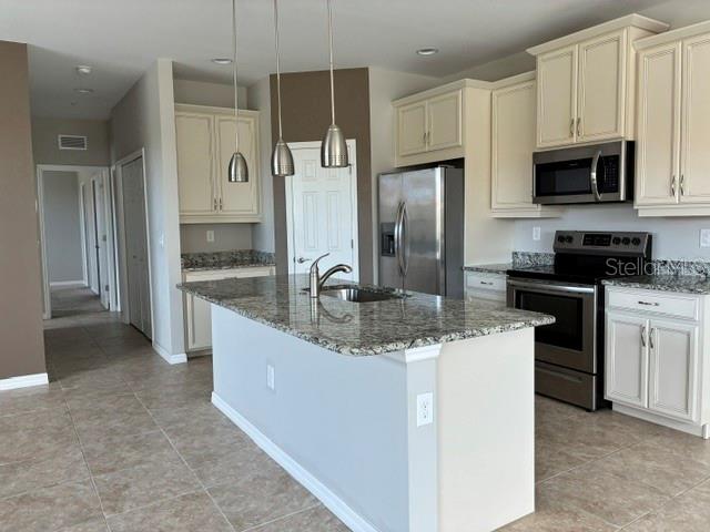 A kitchen features a granite-topped island, stainless steel appliances, and off-white cabinetry — 4219 FRONTIER WAY UNIT 105, OSPREY, FL