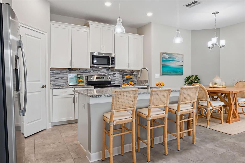 A kitchen features white cabinets, granite countertops, a tiled backsplash, and a breakfast bar island — 3464 EMBERS LANE, CLERMONT, FL