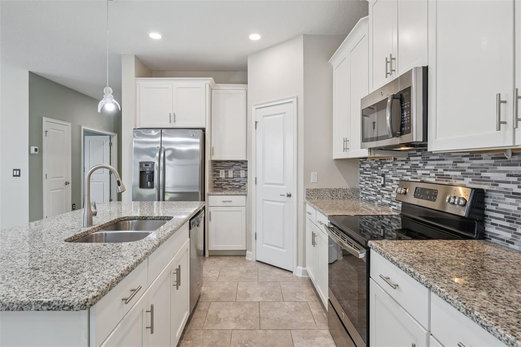 A kitchen with white cabinets, granite countertops, stainless steel appliances, and a tiled backsplash — 3464 EMBERS LANE, CLERMONT, FL