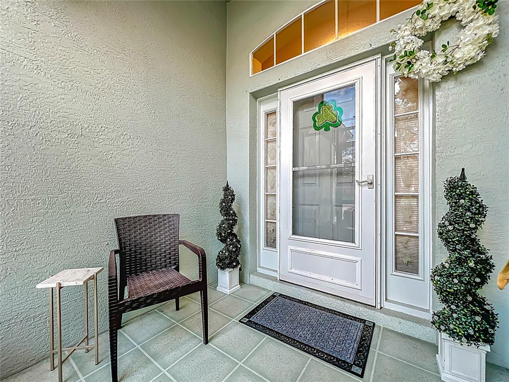 A covered entryway features a front door with sidelights, a chair, and two topiary plants — 4334 HAMMERSMITH DRIVE, CLERMONT, FL