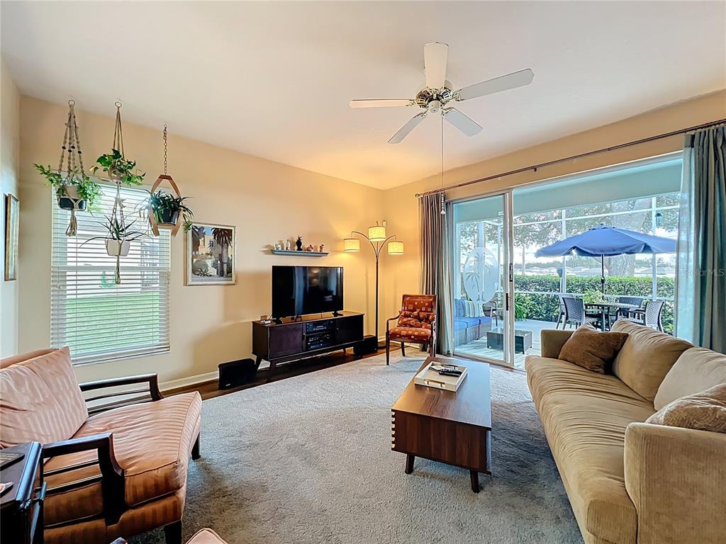 A living room features a beige sofa, patterned armchair, television console, and sliding glass doors — 4334 HAMMERSMITH DRIVE, CLERMONT, FL