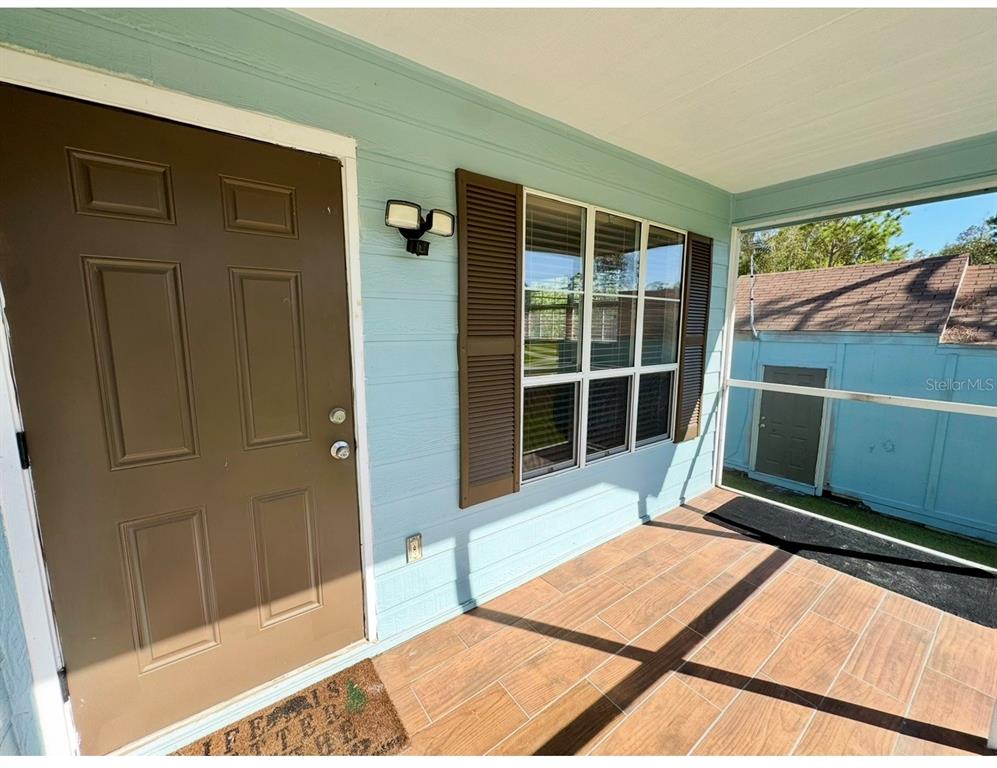 A covered porch with light blue siding, a brown door, and wood-look tile flooring — 12109 PLATANO DRIVE, PUNTA GORDA, FL