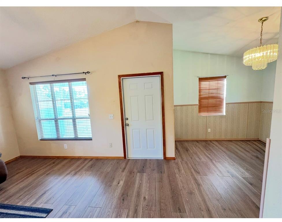A living room with wood-look flooring, a vaulted ceiling, a window, and an adjacent dining area — 12109 PLATANO DRIVE, PUNTA GORDA, FL