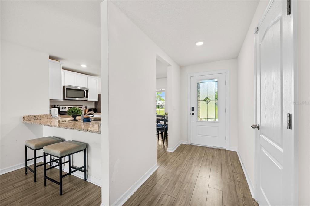 An entryway with wood-look flooring leads to a white front door and a kitchen breakfast bar — 1602 SALADINO STREET SE, PALM BAY, FL