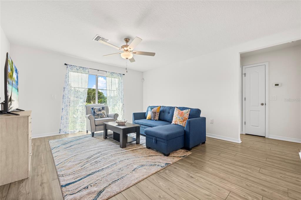 A living room features a blue sectional sofa, a patterned area rug, and wood-look flooring — 1602 SALADINO STREET SE, PALM BAY, FL
