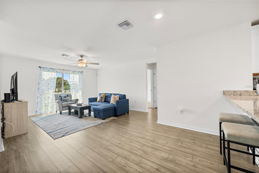 A living room with light wood-look flooring, a blue sectional sofa, and a sliding glass door — 1602 SALADINO STREET SE, PALM BAY, FL