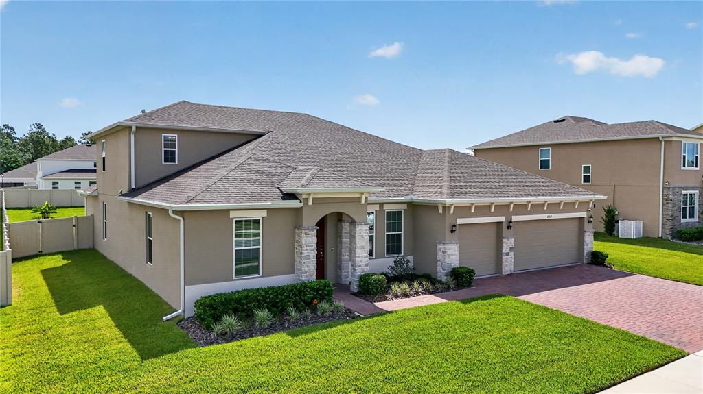 A tan, single-story suburban house with a stone-accented entryway and a brick-paved driveway — 4937 GOLDEN ZENITH WAY, MOUNT DORA, FL