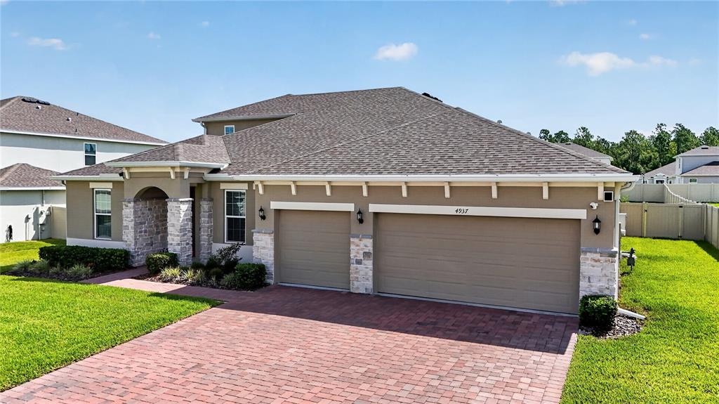 A tan house with a brick driveway, stone accents, and a three-car garage — 4937 GOLDEN ZENITH WAY, MOUNT DORA, FL