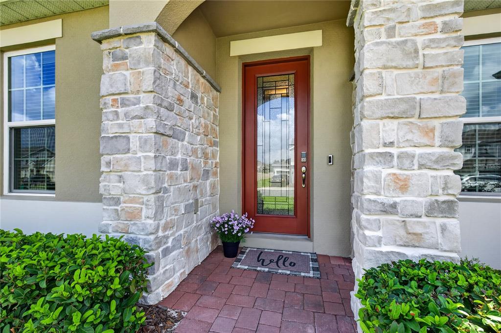 A red front door with a glass insert sits between two stone-clad pillars — 4937 GOLDEN ZENITH WAY, MOUNT DORA, FL