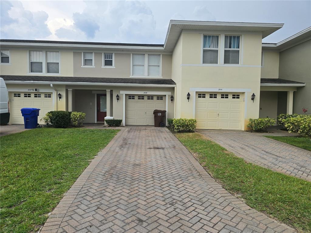 A row of three attached townhomes with paved driveways, garages, and light-colored stucco exteriors — 2039 CYPRESS BAY BOULEVARD, KISSIMMEE, FL