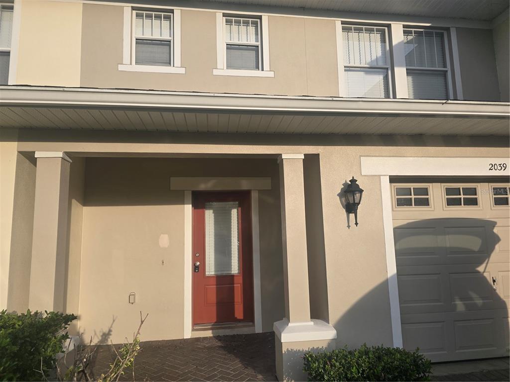 The exterior of a two-story townhouse features a red front door and a garage — 2039 CYPRESS BAY BOULEVARD, KISSIMMEE, FL