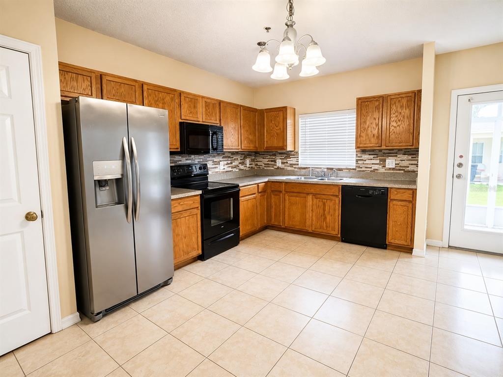 A kitchen features oak cabinets, black appliances, a stainless steel refrigerator, and light tile flooring — 2039 CYPRESS BAY BOULEVARD, KISSIMMEE, FL