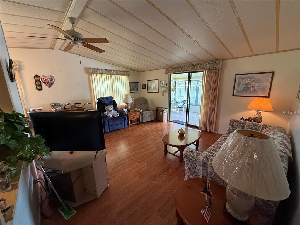 A living room features wood-look flooring, a ceiling fan, a floral sofa, and sliding glass doors — 1532 W SCHWARTZ BOULEVARD, LADY LAKE, FL
