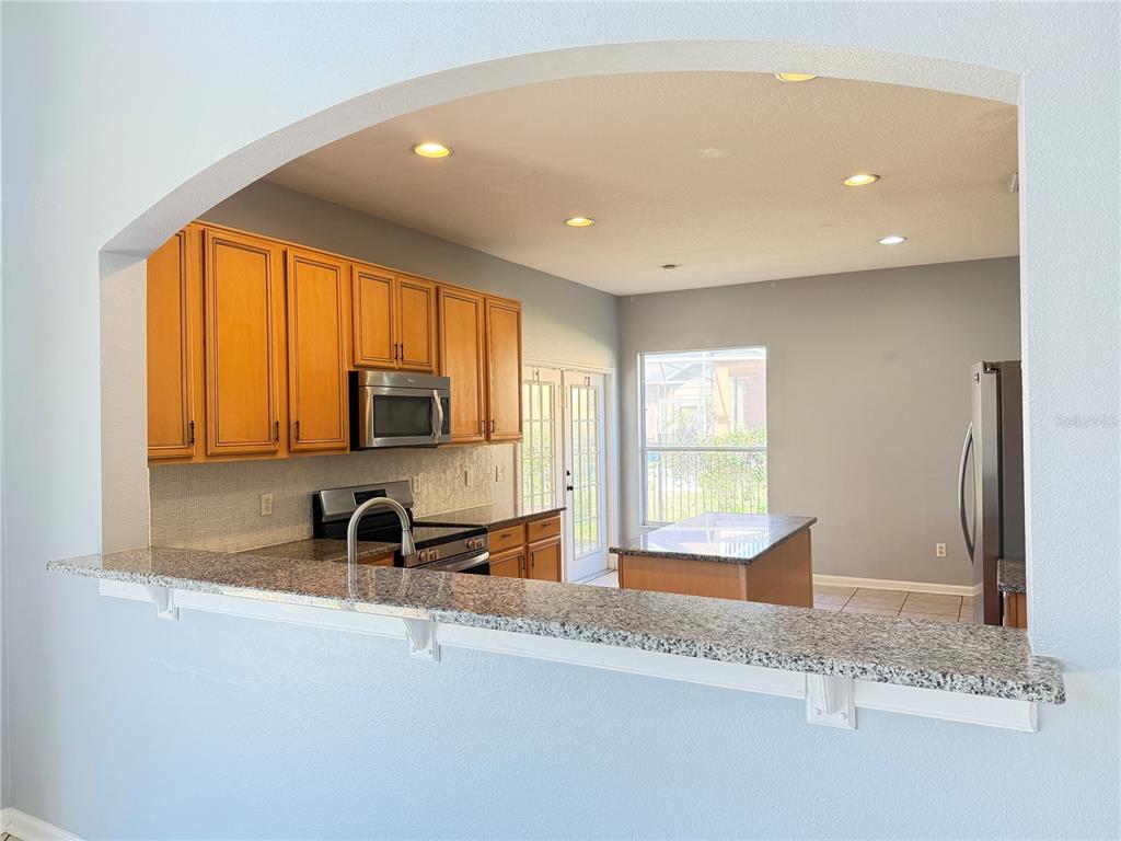 A kitchen with wood cabinets, granite countertops, and a breakfast bar viewed through an archway — 706 STRIHAL LOOP, WINTER GARDEN, FL