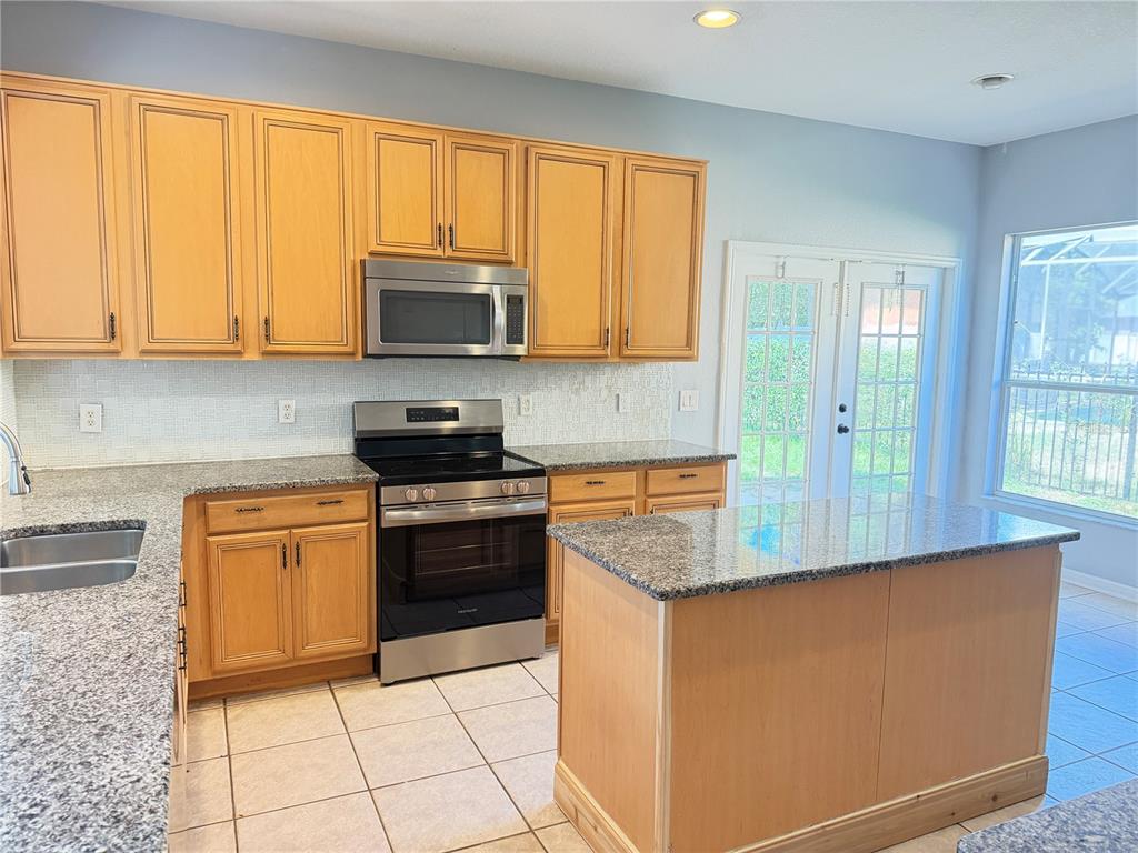 A kitchen features light wood cabinets, granite countertops, stainless steel appliances, and a center island — 706 STRIHAL LOOP, WINTER GARDEN, FL