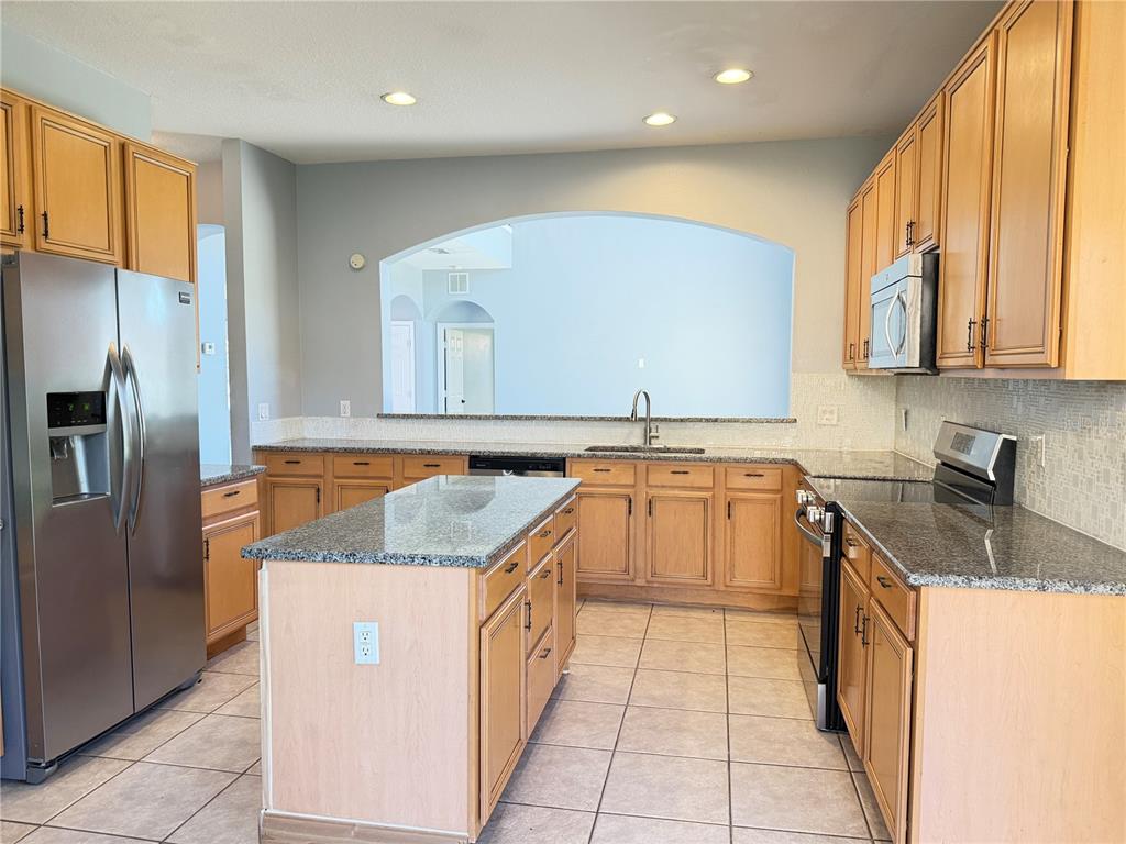 A kitchen features light wood cabinets, granite countertops, a center island, and stainless steel appliances — 706 STRIHAL LOOP, WINTER GARDEN, FL