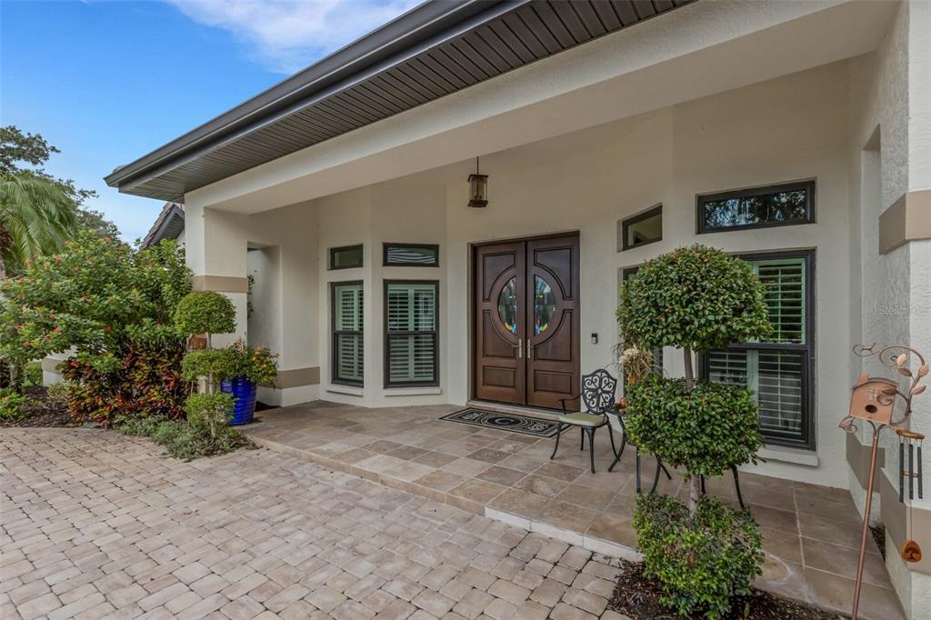 A paved driveway leads to the covered front porch and double wooden doors of a house — 7732 DONALD ROSS ROAD W, SARASOTA, FL